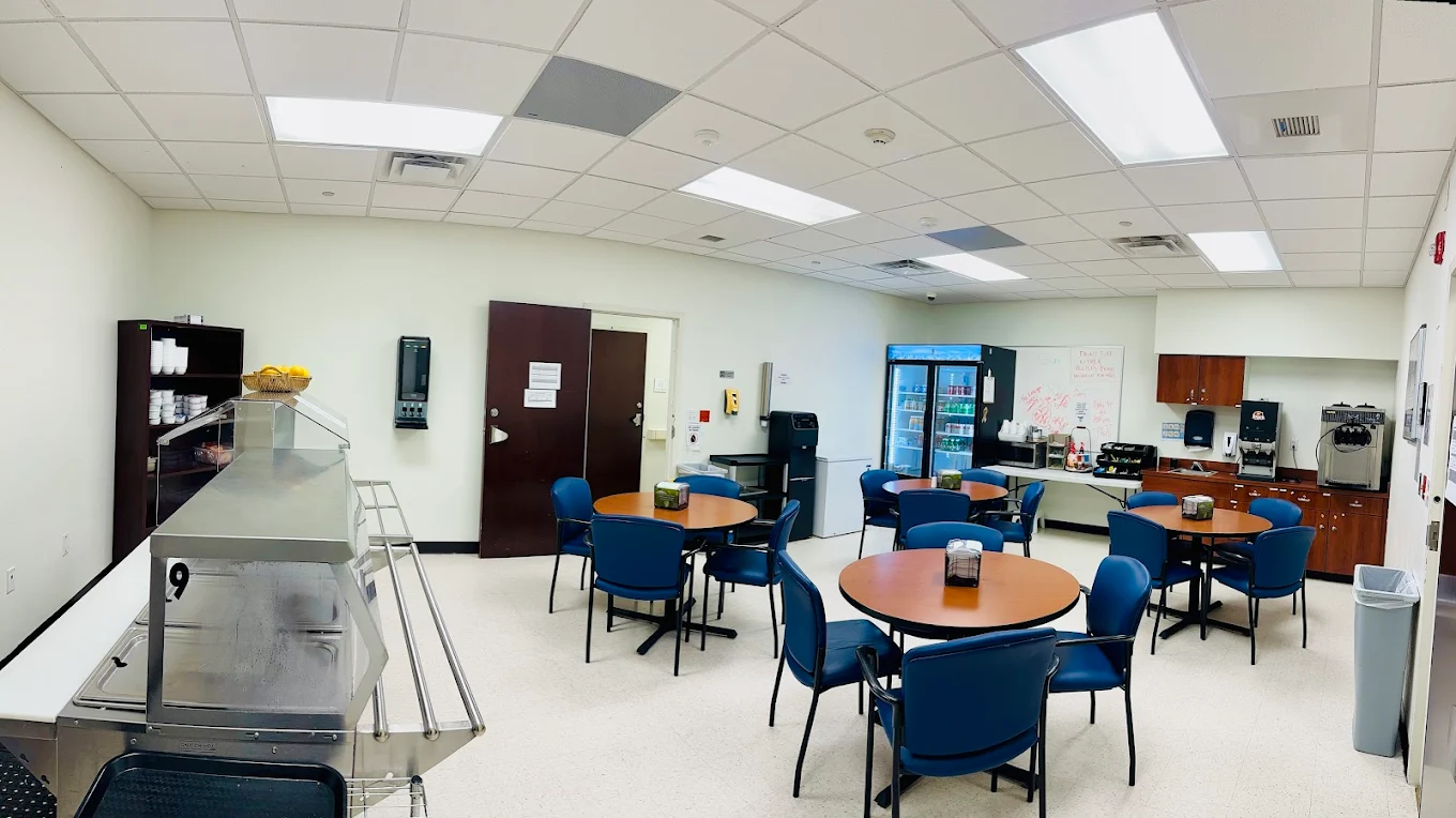 Round dining tables with blue chairs in a cafeteria-style space with food service counter