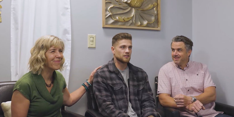 Three people are seated in a supportive environment, with one person placing a reassuring hand on another's shoulder, showing care and understanding.