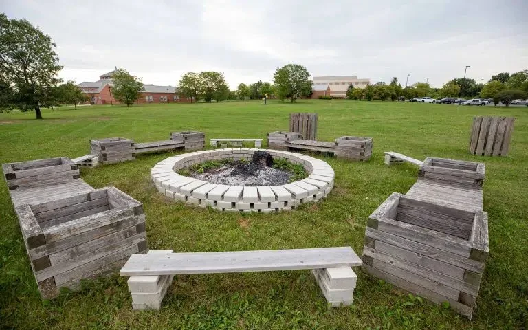 Outdoor fire pit surrounded by wooden benches on grassy grounds