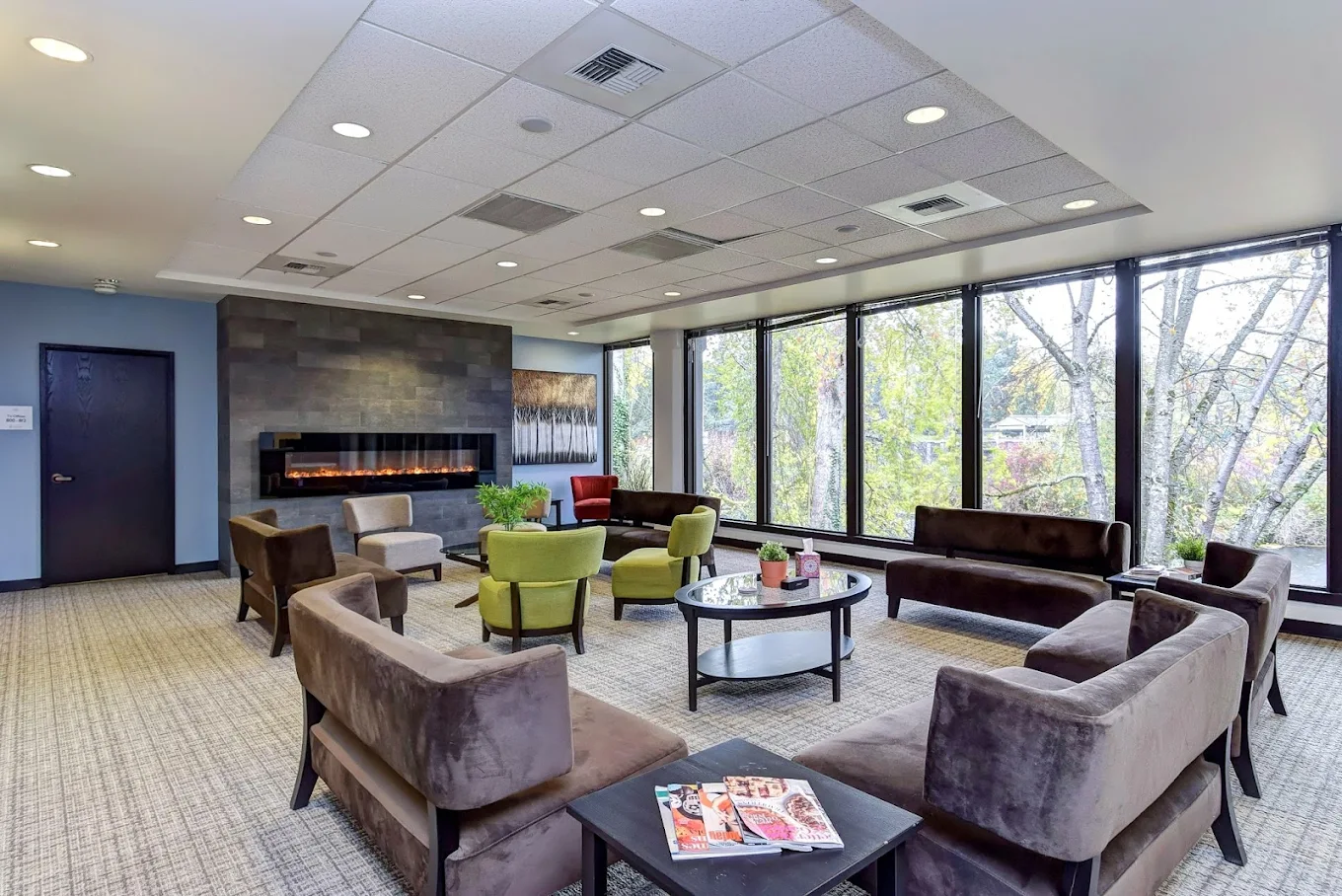 Spacious communal lounge with floor-to-ceiling windows, modern fireplace, and a variety of seating including armchairs and sofas