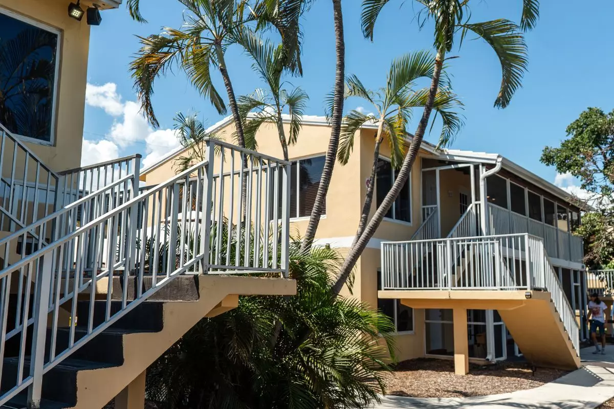 Two-story yellow facility building with stair access and palms