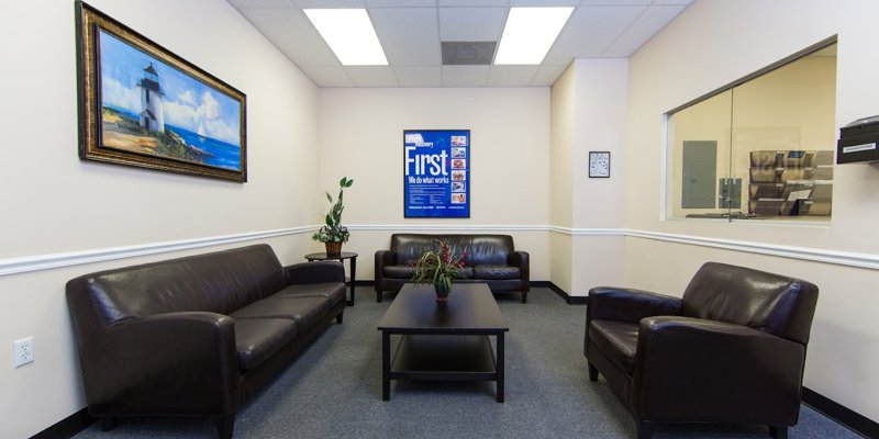  A comfortable waiting area with dark leather sofas, a coffee table, and calming artwork on the walls, offering a welcoming and relaxed atmosphere.