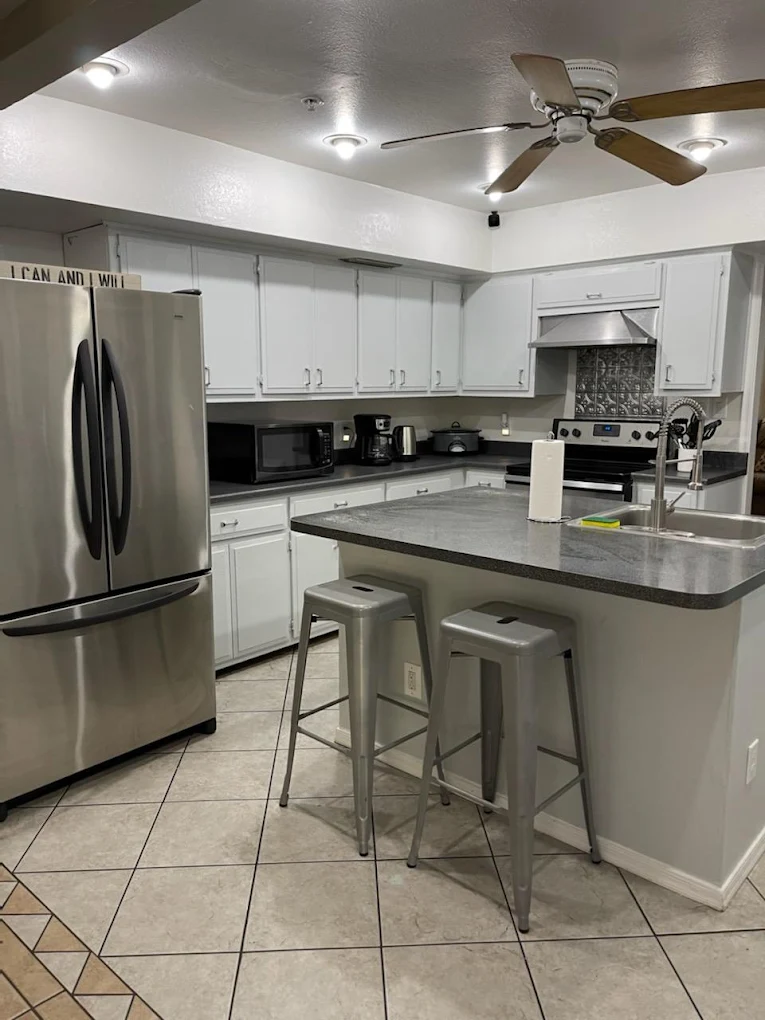 Modern kitchen with stainless steel appliances, white cabinets, a center island with stools, and ceiling fan lighting