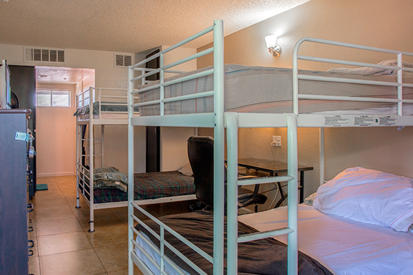 Room with multiple white bunk beds, desk, and tiled floor