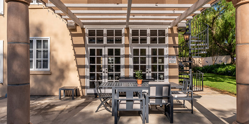 Charming outdoor patio with a pergola, elegant columns, and modern dining furniture, perfect for relaxing and enjoying the sunny weather.