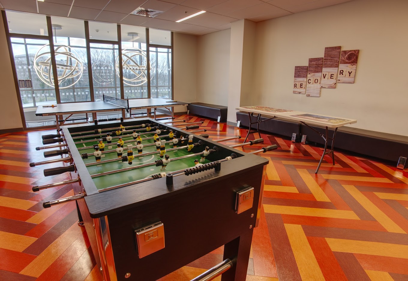 Recreation room with a pingpong and foosball table with seating along wall.