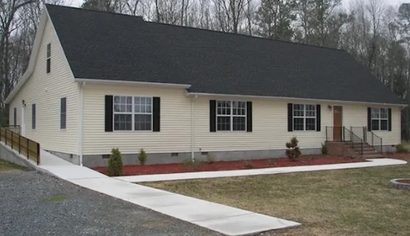 One-story beige home with sidewalk and black roof