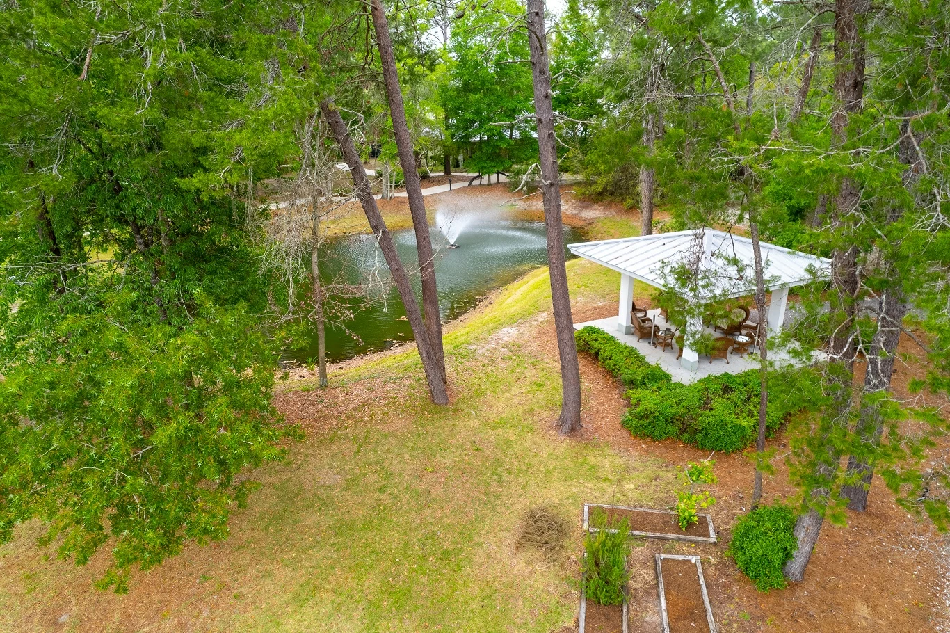 Peaceful pond with fountain and covered gazebo surrounded by trees and landscaped grounds