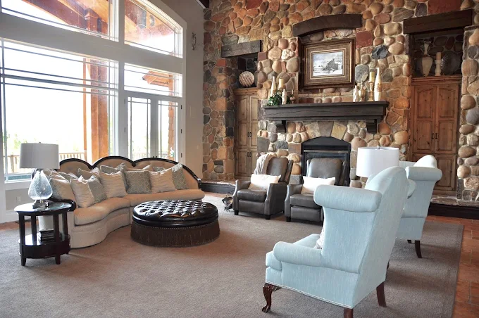 Tall stone fireplace and plush seating under large windows