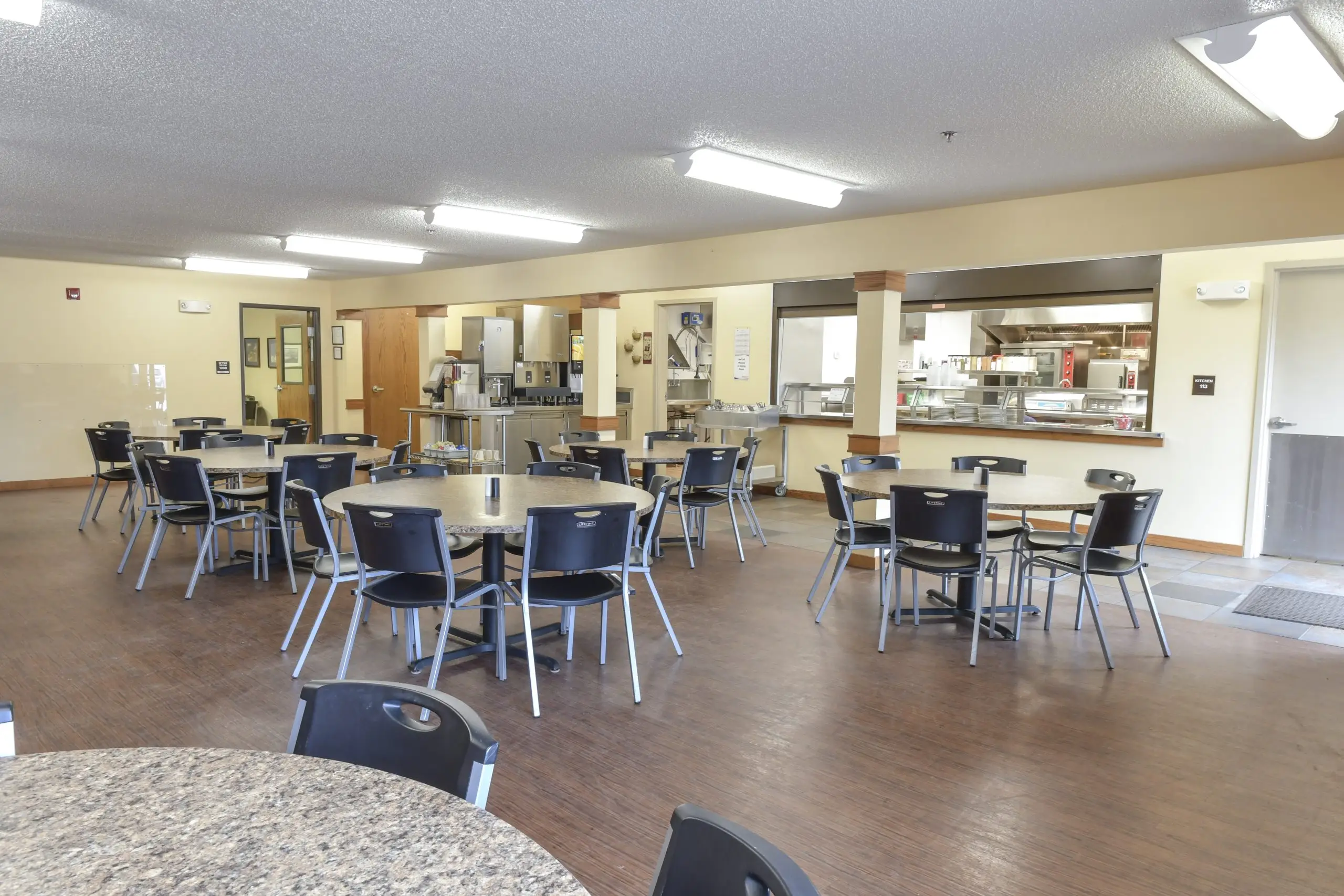 Bright cafeteria with round tables and serving area