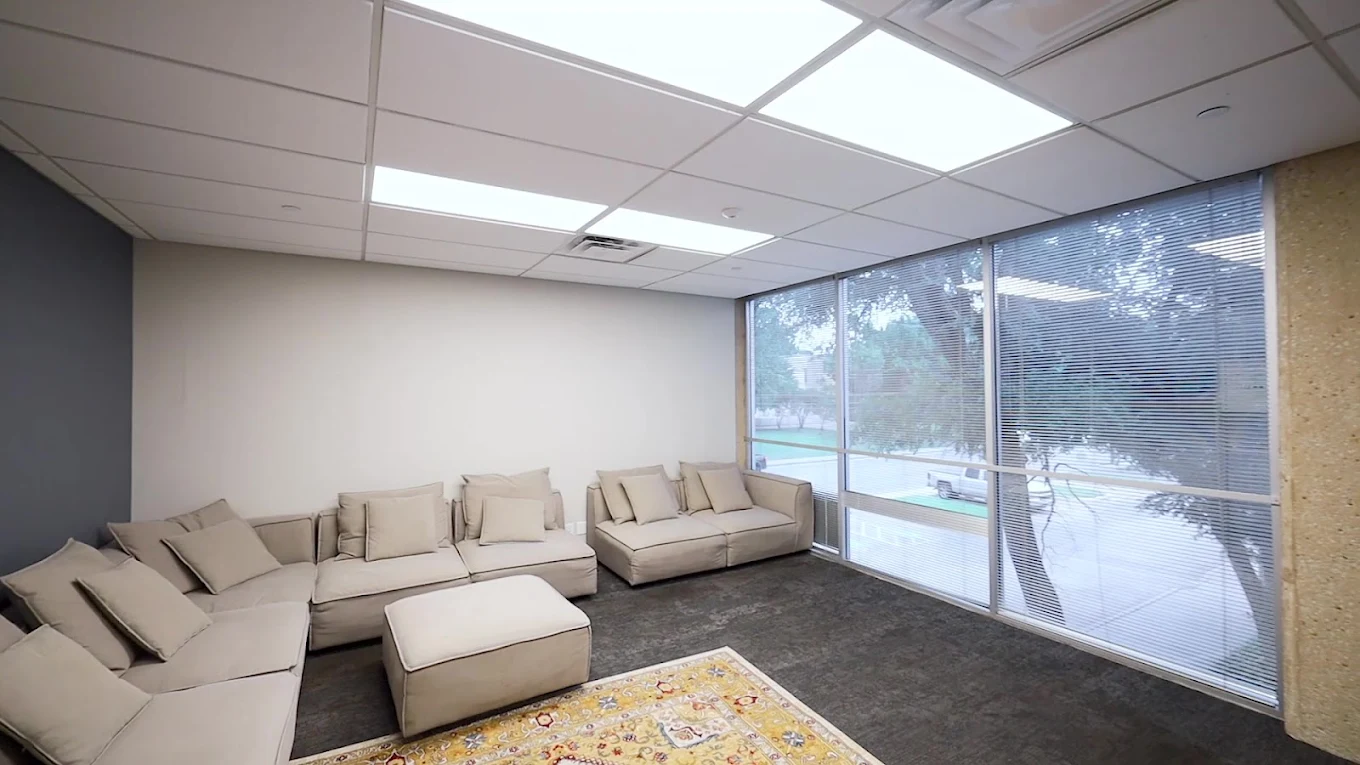 Bright lounge with cream sectional seating, large windows overlooking the courtyard, dark carpeting, and a patterned area rug