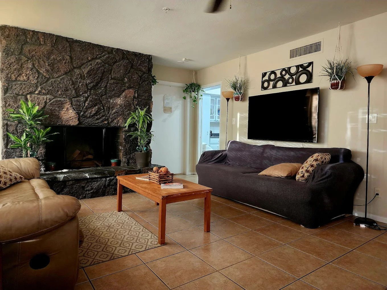 Comfortable living room with leather sofa, dark fabric couch, coffee table, stone fireplace, and wall-mounted TV