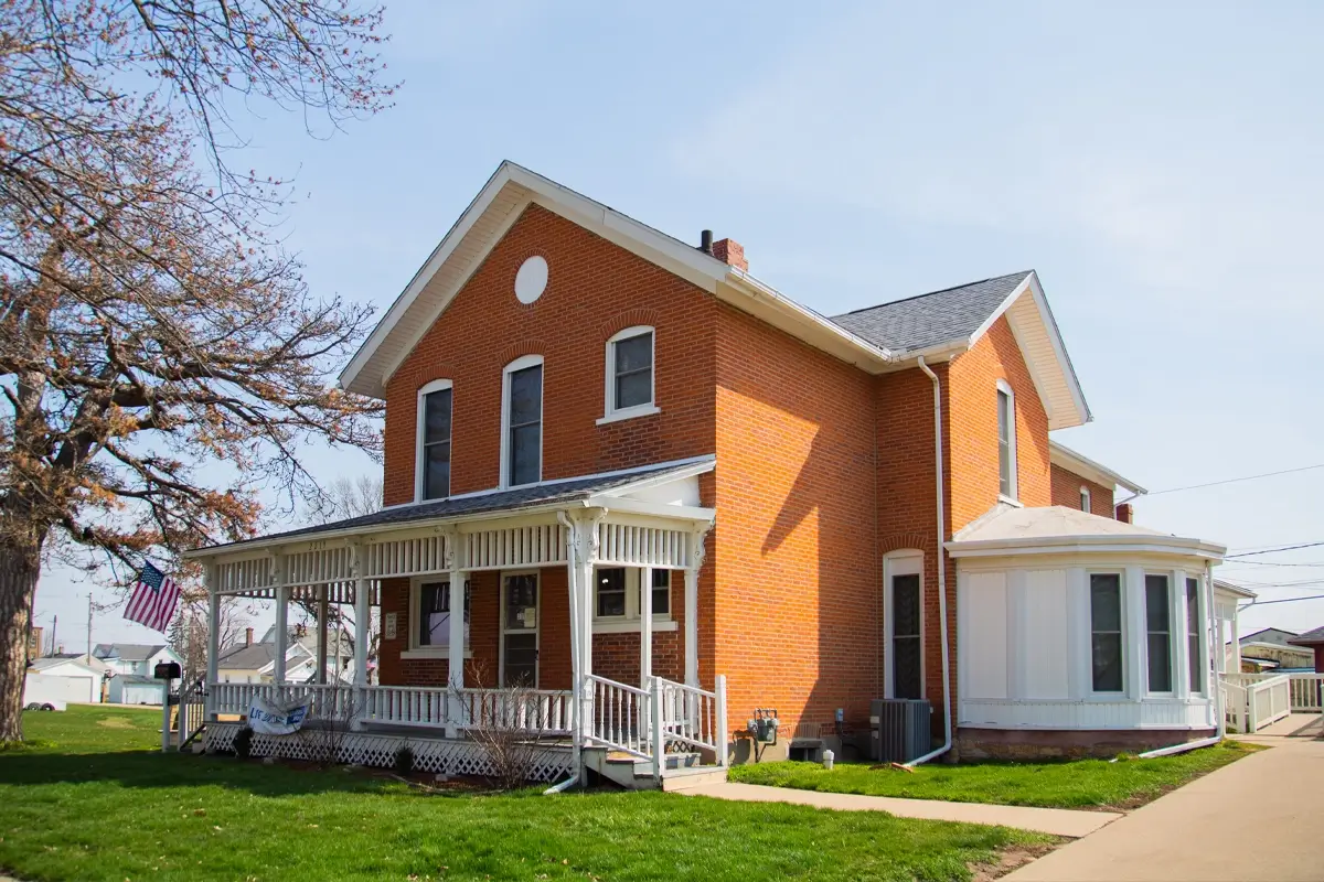 Brick residential facility with wraparound porch and large front lawn.