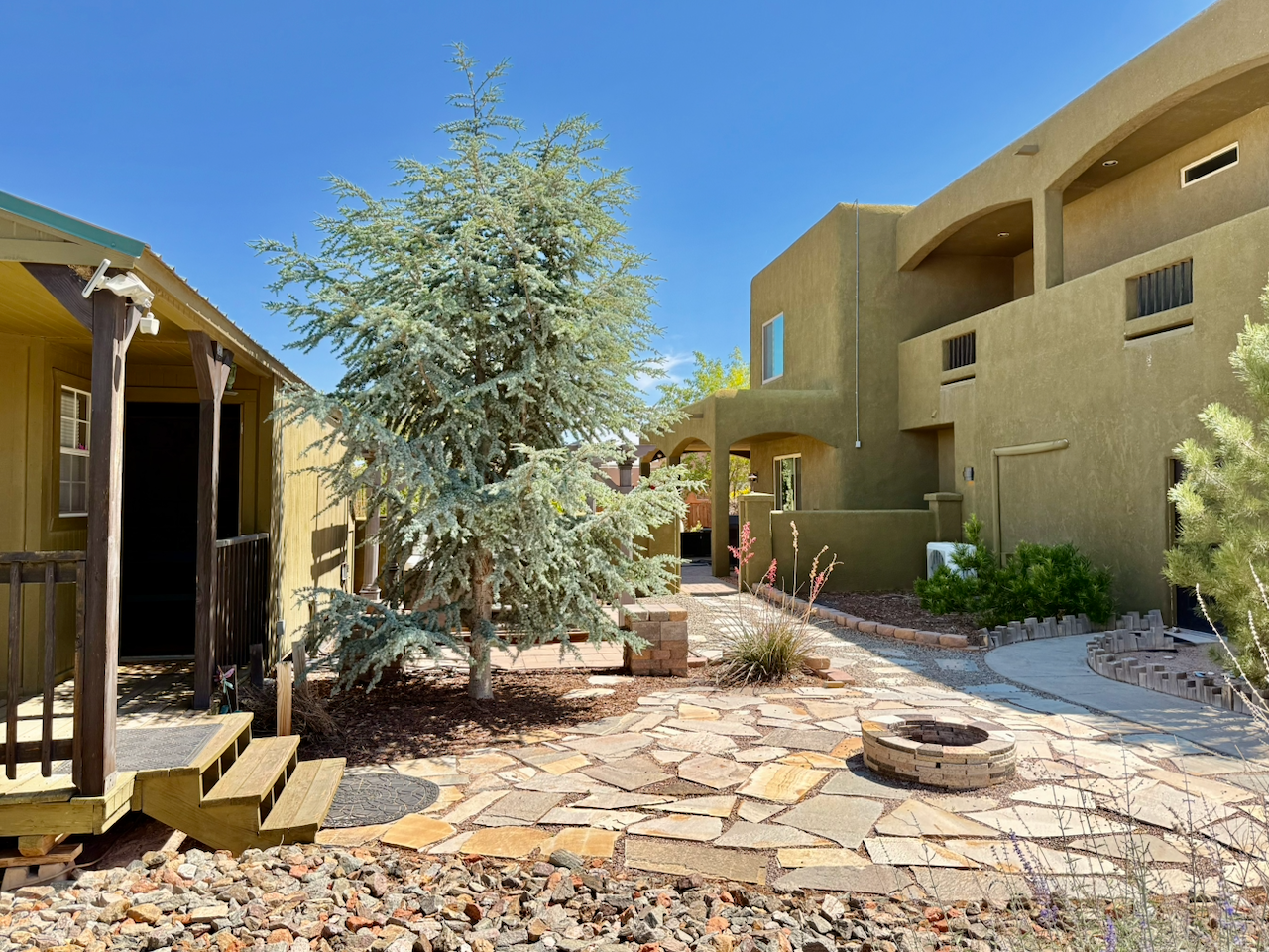 Landscaped courtyard with stone pathways, mature trees, fire pit, and outdoor structures