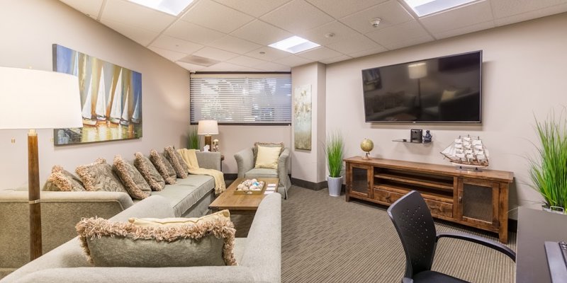  A cozy, well-lit lounge area featuring plush seating, a large TV, and serene decor, creating a comfortable and inviting space for relaxation.