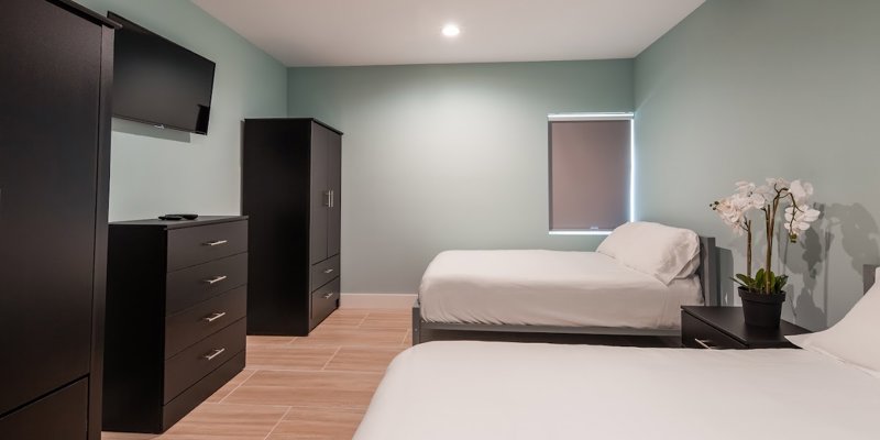 A calm, neatly arranged bedroom with two cozy beds, modern black furniture, a TV, and soft lighting.