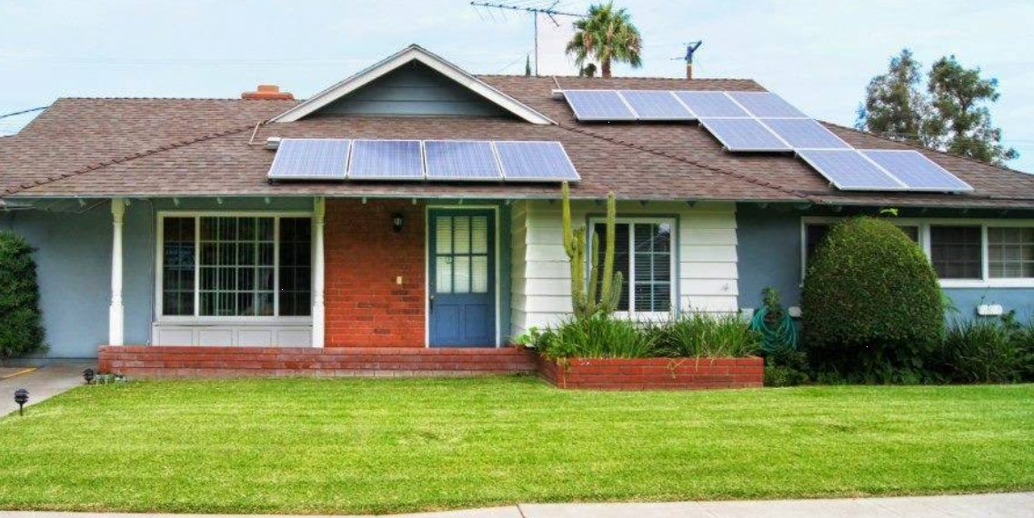 Single-story home with solar panels on roof and green lawn in front