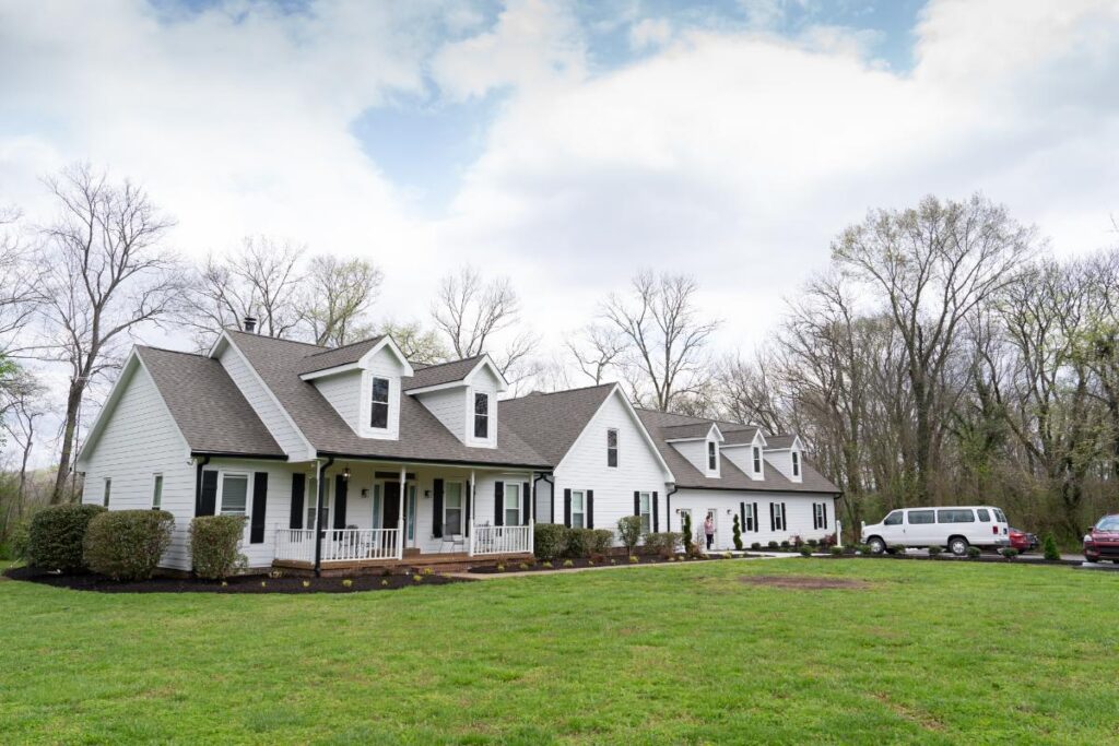 White residential building with dormer windows, front porch, and landscaped lawn