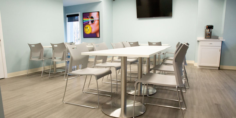  A bright and inviting dining area with sleek tables and chairs, modern artwork, and a TV, offering a comfortable space for meals and socializing.