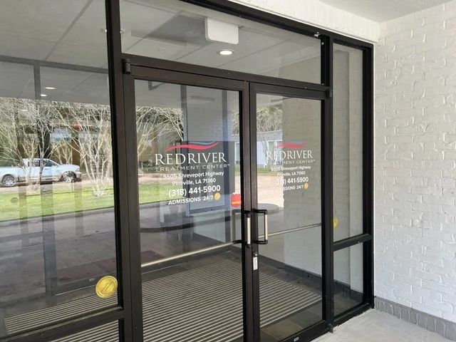 Glass entrance doors at Red River Treatment Center in Pineville with facility name and contact information displayed