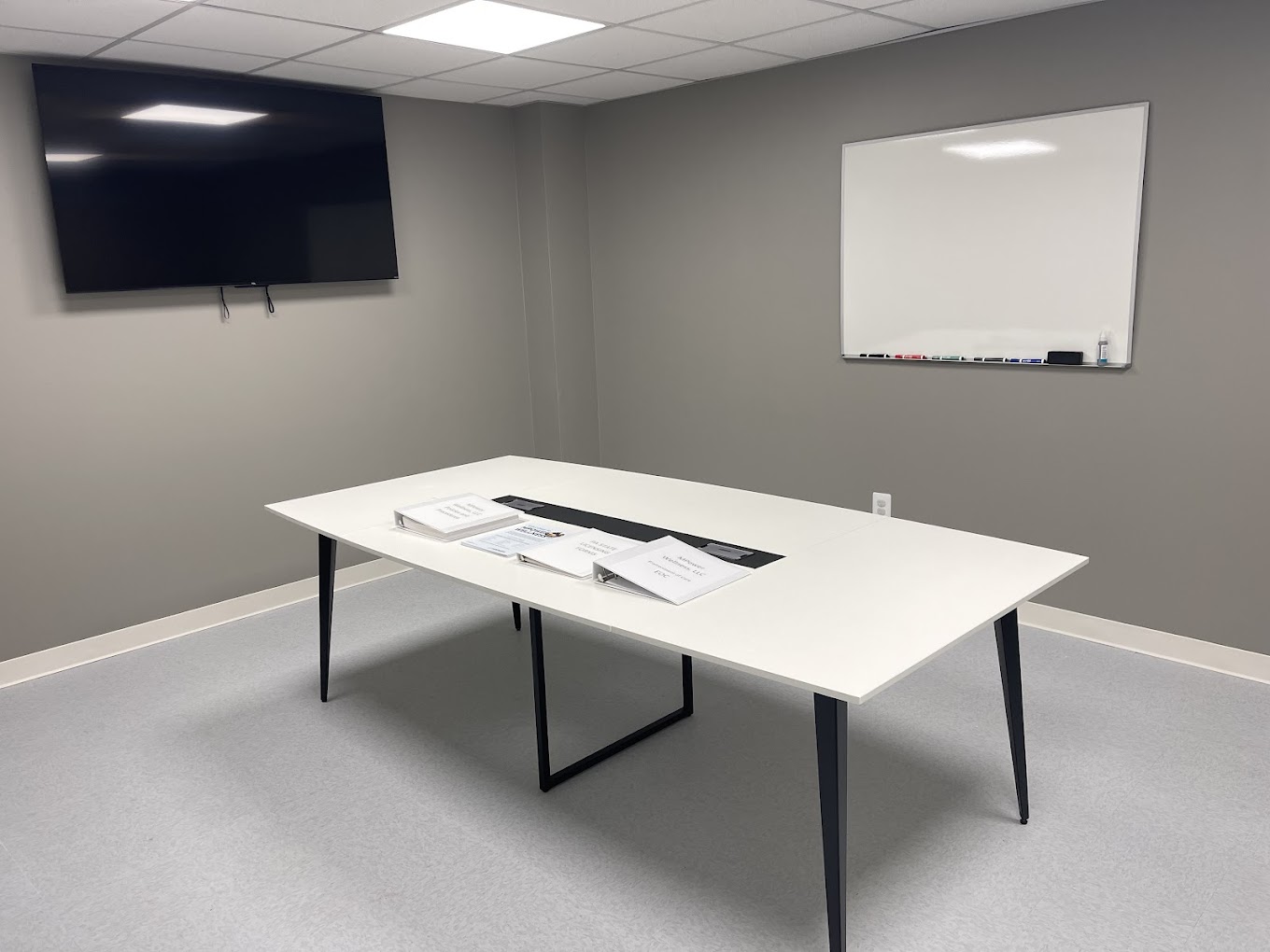A conference room with a white table, TV, and whiteboard.