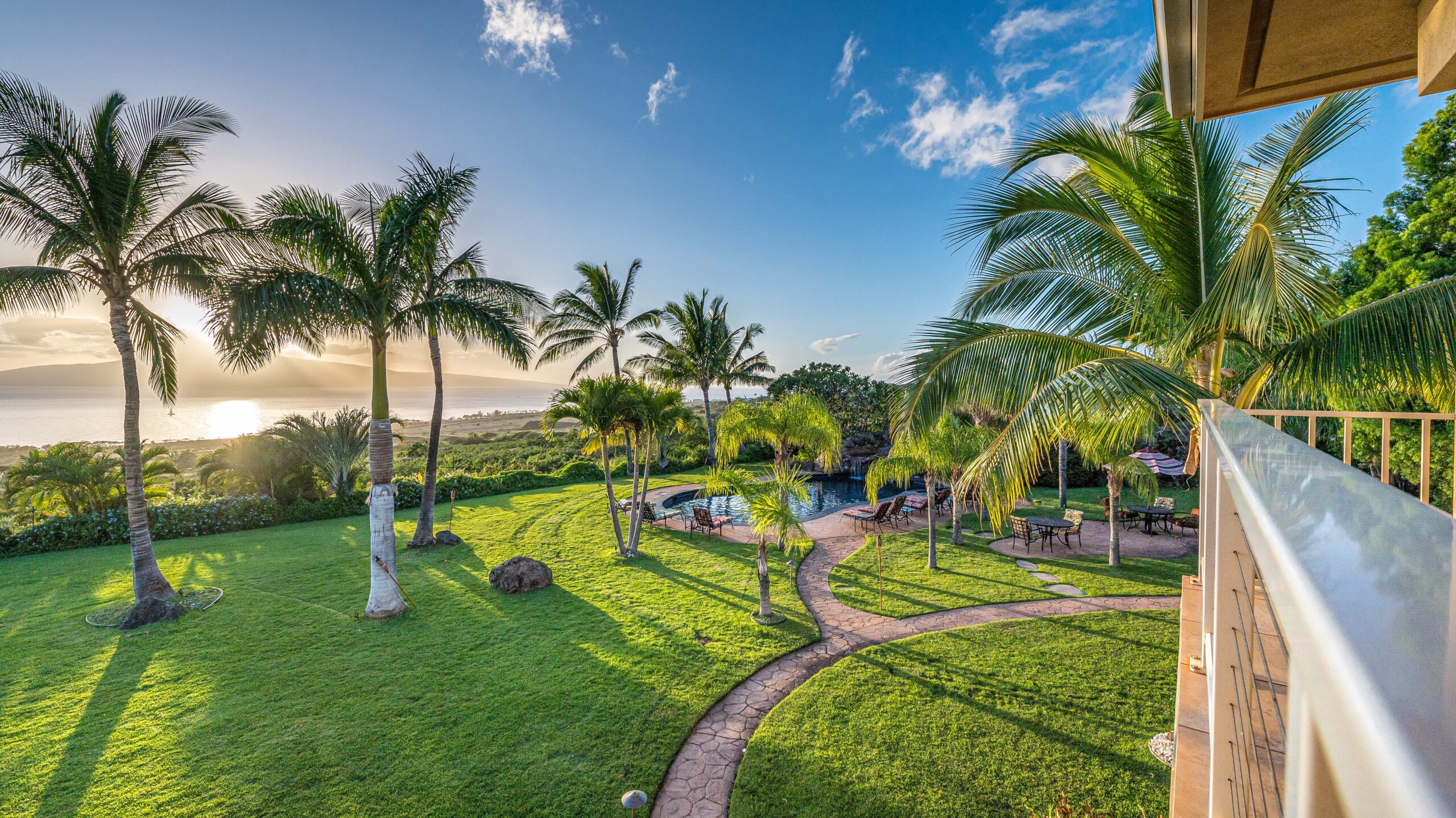 Sunset view over landscaped gardens, walking paths, and the resort-style pool overlooking the ocean
