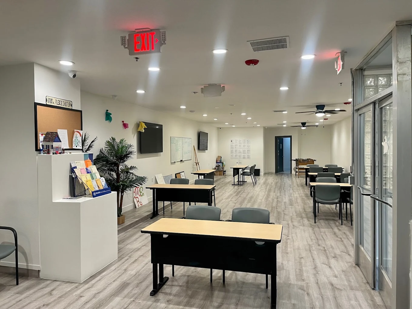 Bright classroom with desks, bulletin board, TVs, and open floor space.