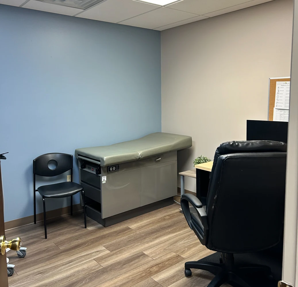 BrightView Health clinical room with examination table, patient chair, workstation, blue accent wall, and wood-look flooring