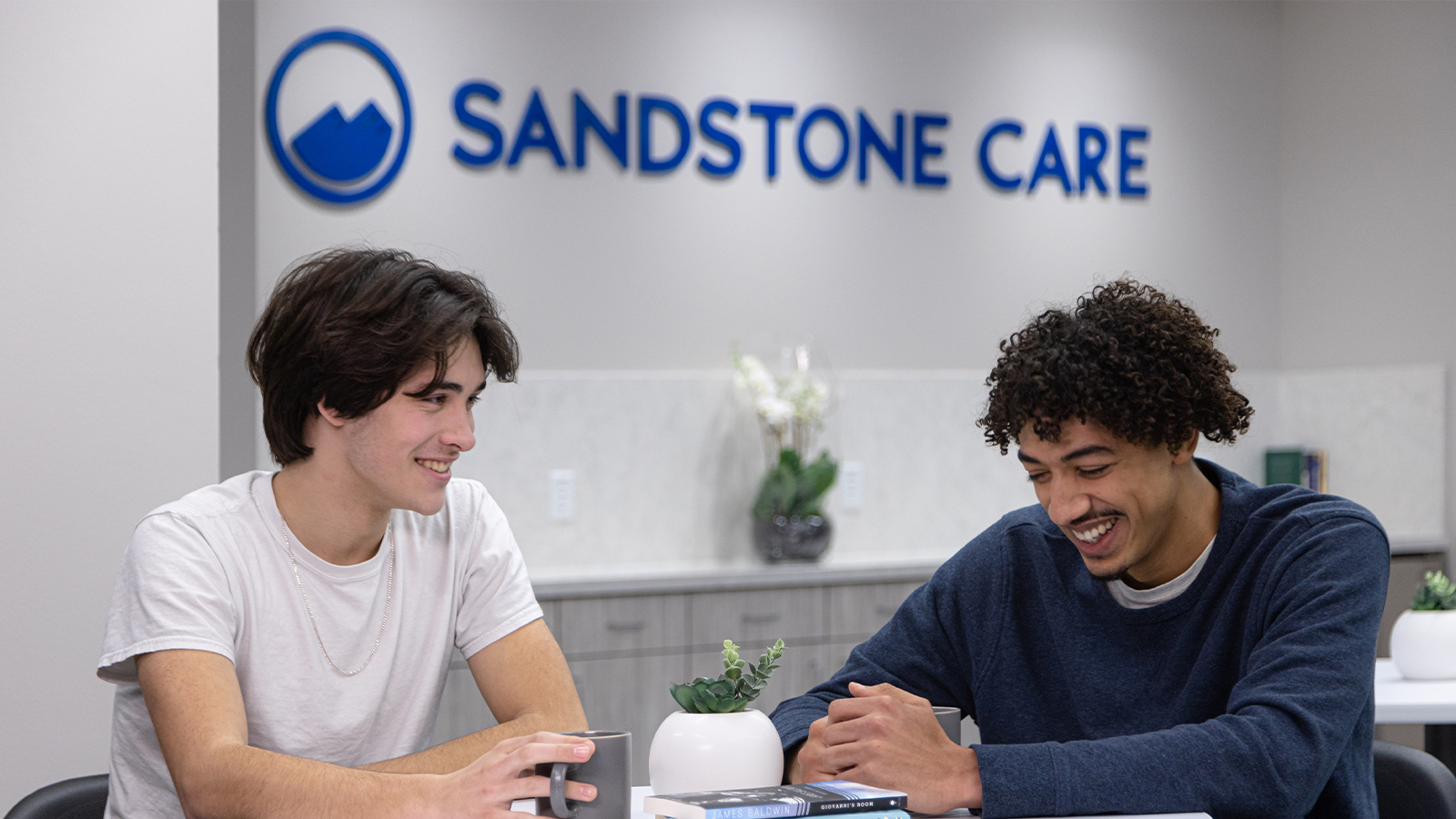 Two young men laughing at a table in a rehab center.