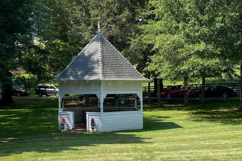White open-air gazebo on lawn surrounded by trees
