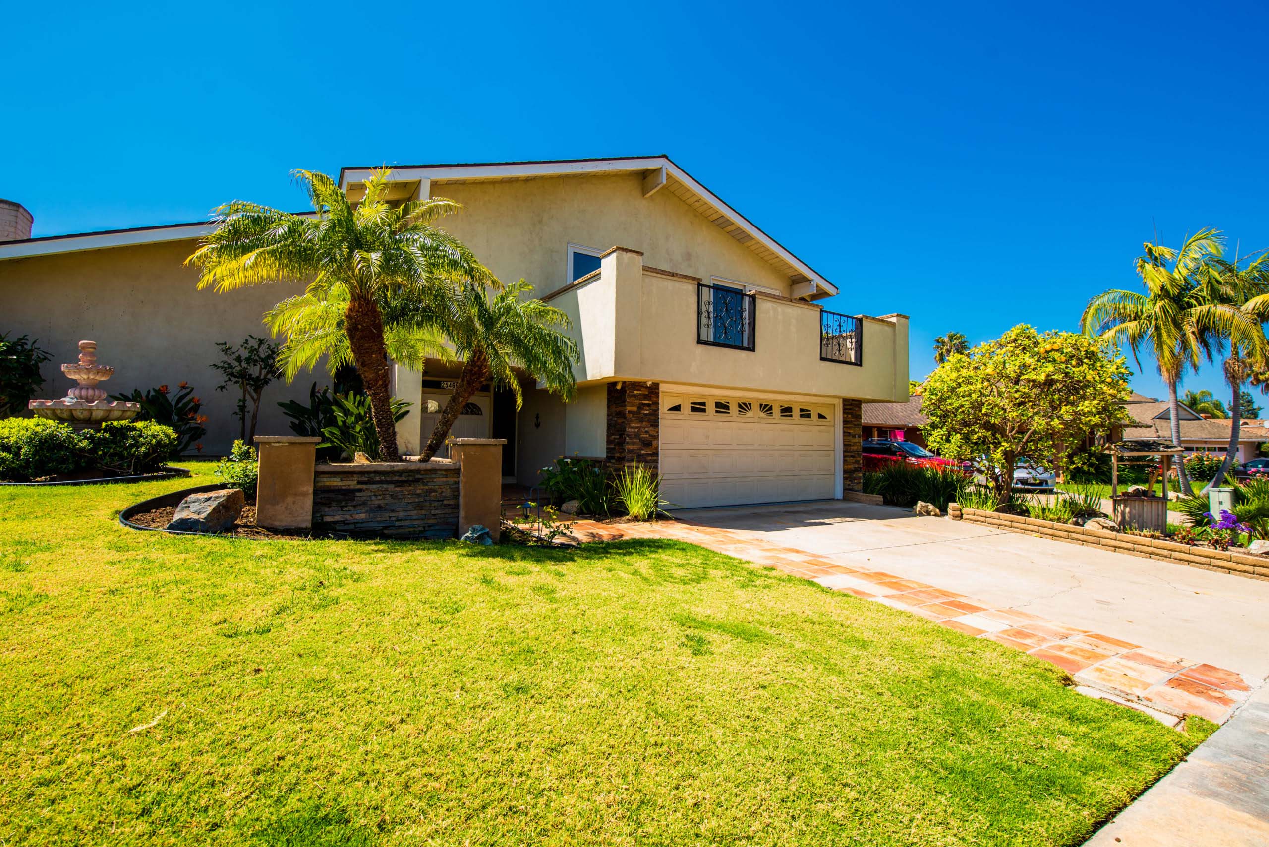 Two-story home with palm trees and green lawn