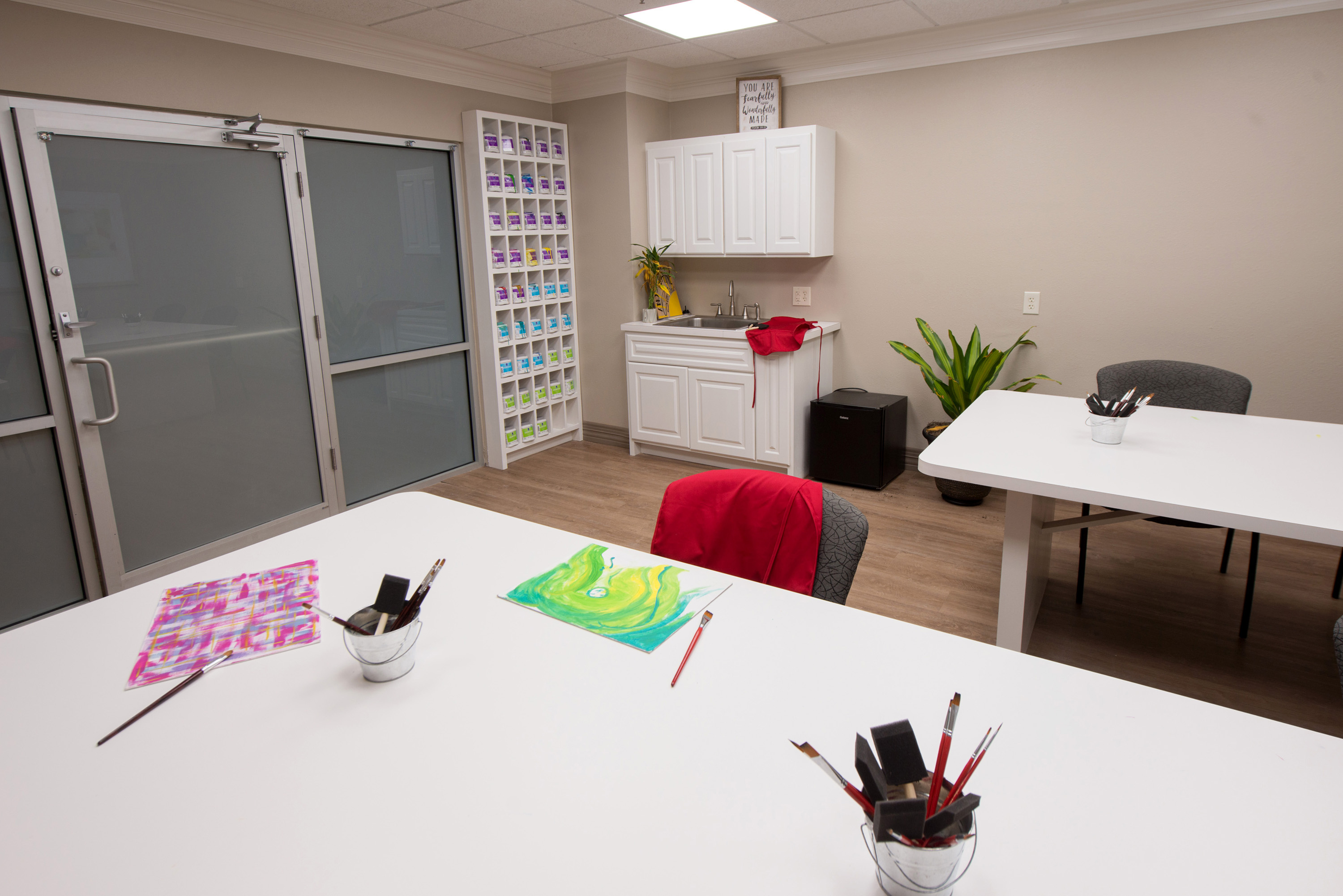 Art room with paint supplies, easels, and white tables