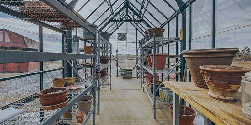 A spacious greenhouse filled with shelves of empty pots, ready for planting, offering a bright, airy environment with views of the farm outside.