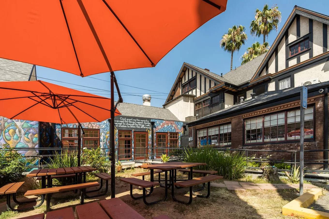 Red picnic tables and umbrellas in shaded garden beside mural wall