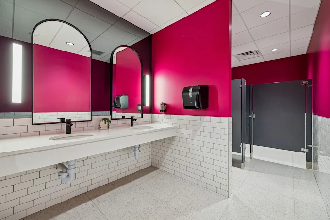 Public restroom with a vibrant pink wall and black framed mirrors.