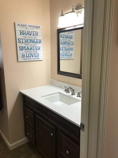 Small bathroom with sink, mirror, and motivational sign.