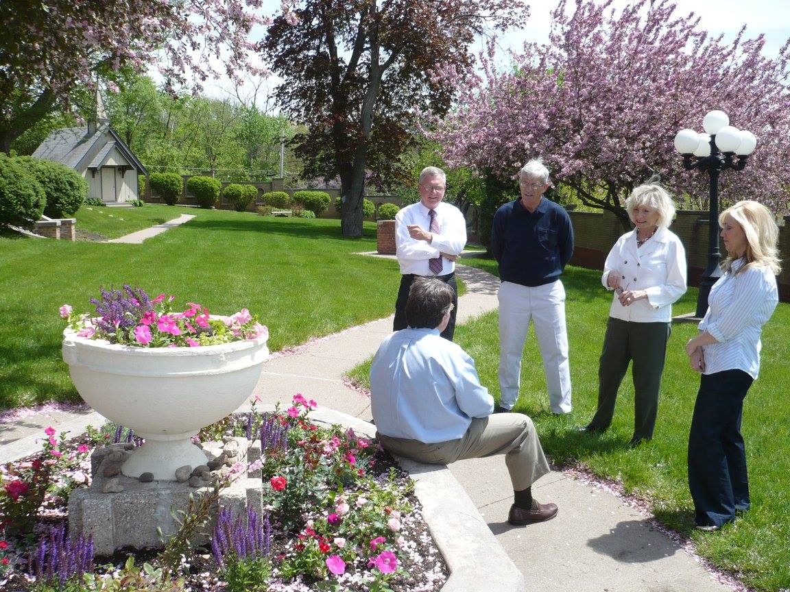 Group of adults chatting in garden near chapel and flowers