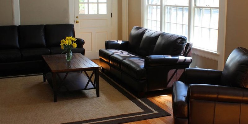  A cozy living room with black leather sofas, a wooden coffee table, and bright natural light from large windows, creating a warm and inviting space.