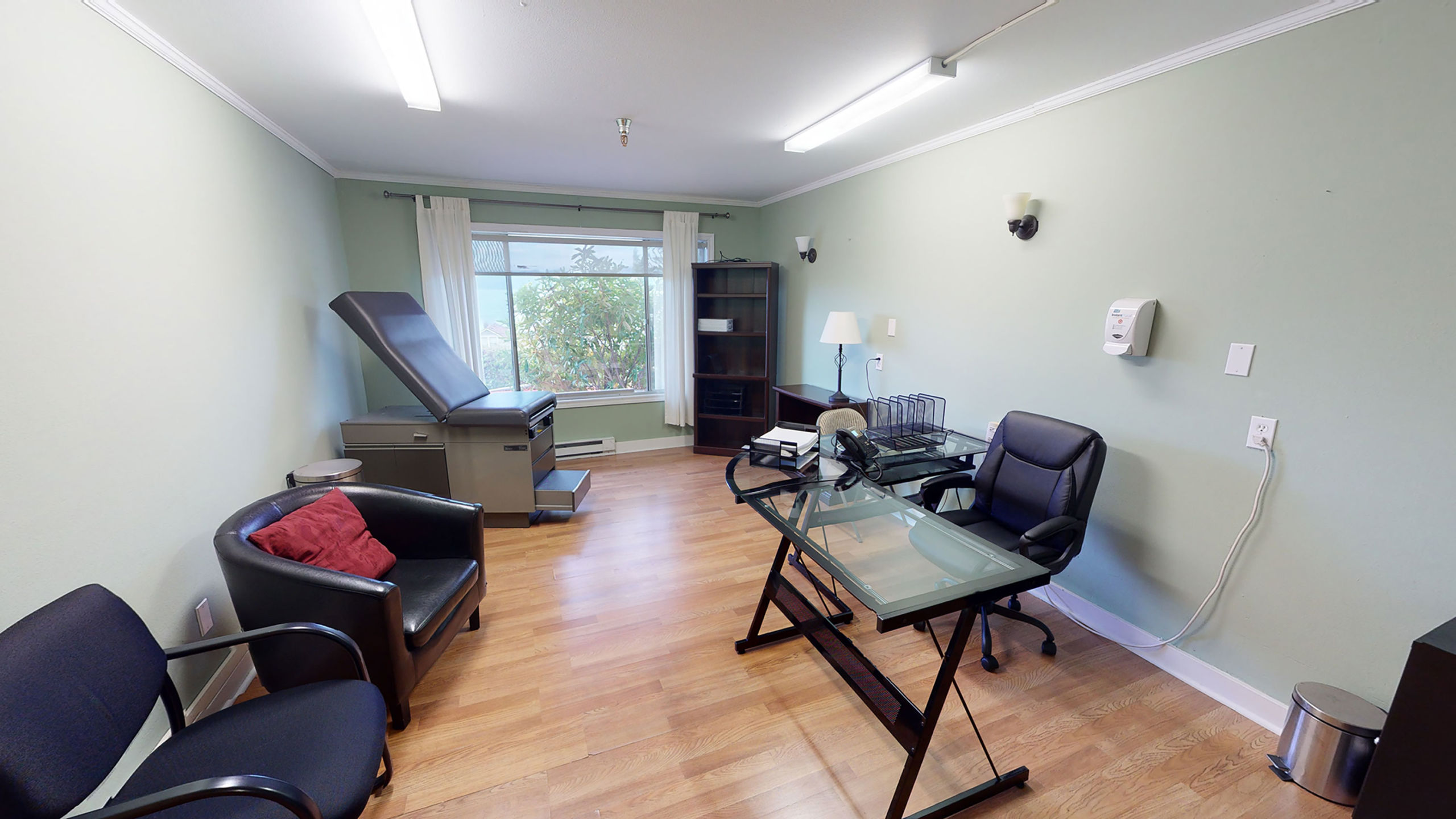 Clinical room with desk, exam table, and guest chairs