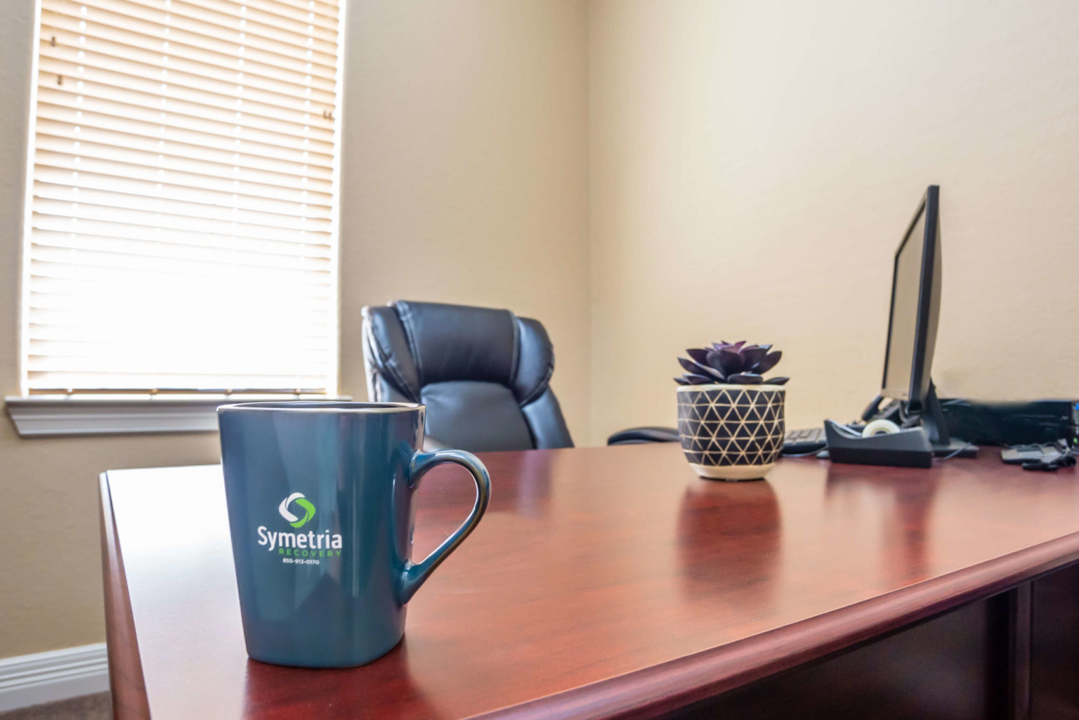 A professional office desk with a Symetria Recovery coffee mug.