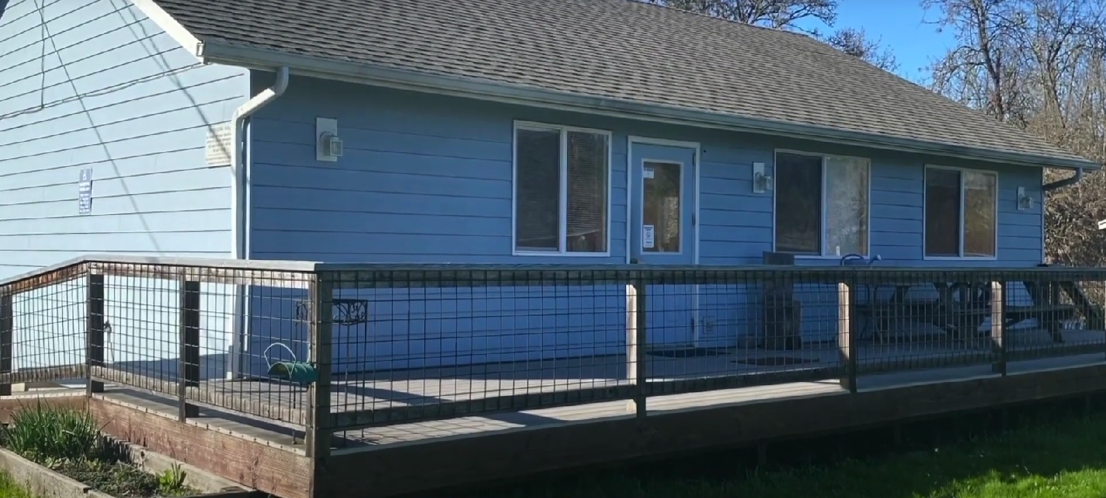 Blue rehab facility with ramp and deck surrounded by greenery