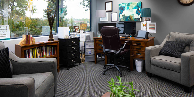  A cozy, well-lit office with comfortable seating, a desk, and a bookshelf filled with books, offering a peaceful and welcoming atmosphere.