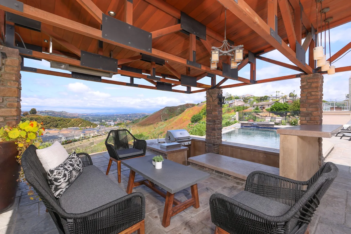 Covered patio with seating, grill, pool, and hillside views