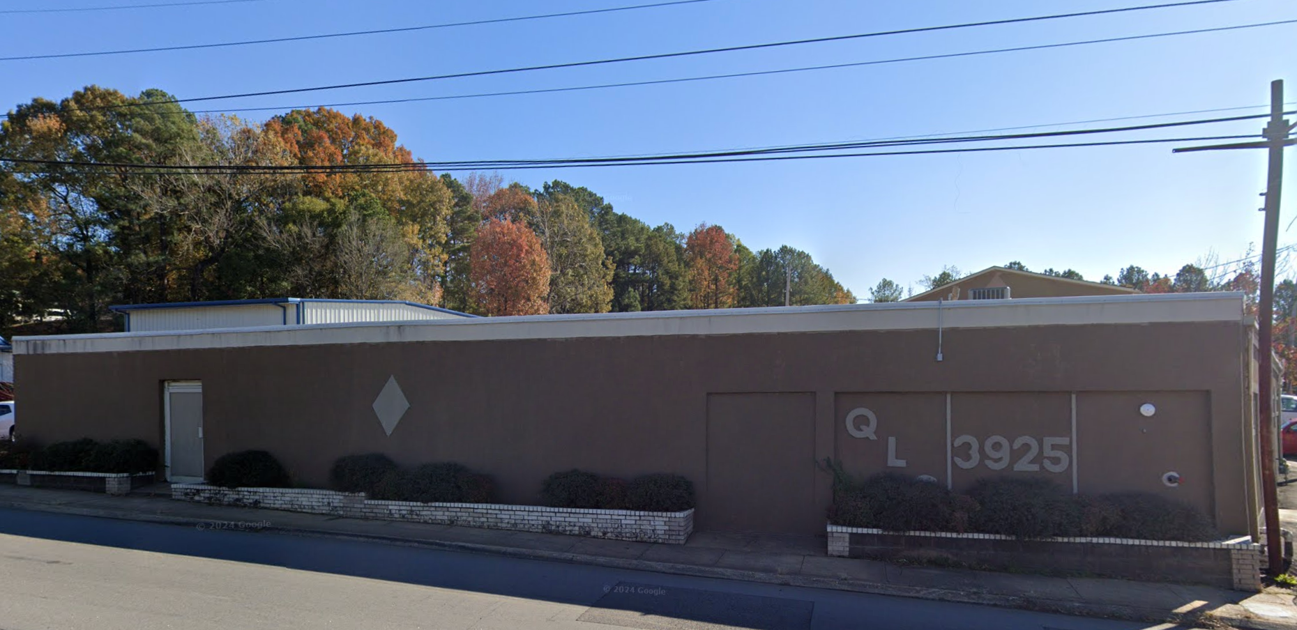 A long, brown building with minimal signage, featuring the address "3925" and "QL" on the wall, with small bushes along the sidewalk.