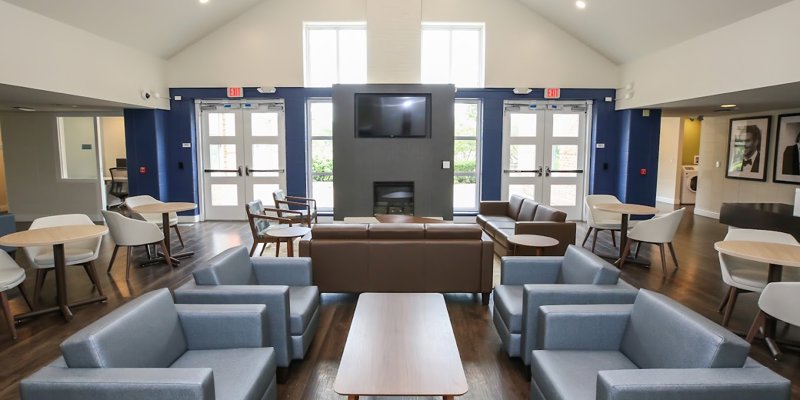 Inviting lounge area with cozy seating, large windows, and a central fireplace under a high ceiling, offering a relaxing, open atmosphere.