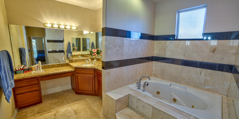 A luxurious bathroom featuring a spacious jacuzzi tub, granite countertops, dual sinks, and warm wooden cabinetry, creating a relaxing ambiance.