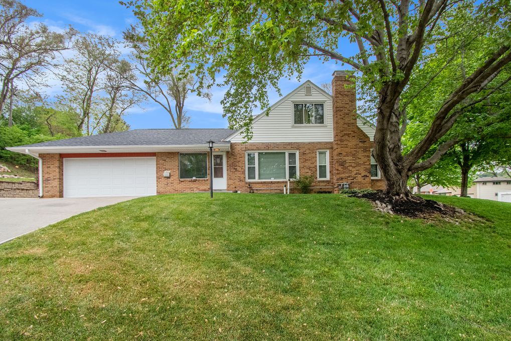 Brick residence with green lawn, large tree, and garage