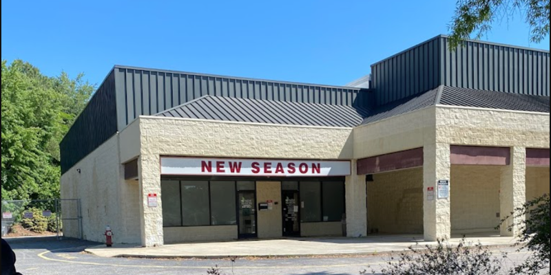  A simple, well-maintained building with the sign "New Season" on the front. The clear skies and surrounding greenery create a calm setting.