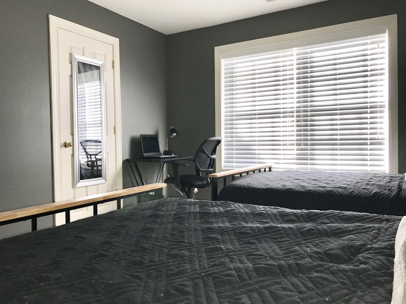 Shared bedroom with two beds, desk, and large window blinds.