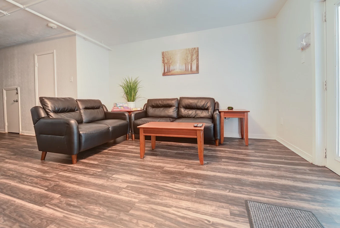 Residential lounge with black leather sofas, wooden coffee and side tables, wood-look flooring, and wall art